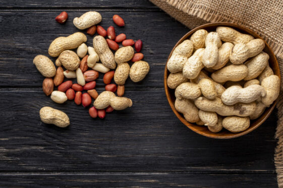 top-view-unshelled-peanuts-bowl-with-peeled-black-wooden-table_